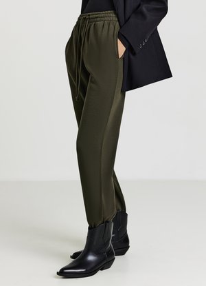 Pantalons de jogging vert olive avec taille élastique, poches latérales et chevilles resserrées, associés à des bottines en cuir noires.