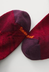 Røde og lilla sokker med teksturert stoff. Har merkevarenavnet "Smartwool" i oransje på kanten. Ankellengde med forsterket tå.