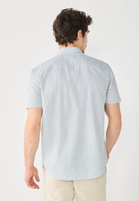 Chemise à manches courtes à boutons en bleu clair avec des rayures verticales blanches. Comprend un col de chemise, une emmanchure au dos et un ourlet arrondi.