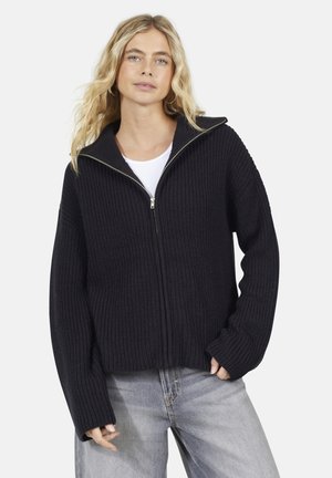 Pull en maille noire chunky avec un col haut, une fermeture éclair et des manches longues. Sa texture côtelée et sa coupe courte lui confèrent une touche d'unicité.
