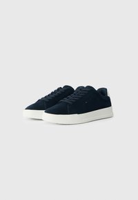 Zapatillas de ante azul marino con suelas de goma blanca, que cuentan con cordones redondos y una textura suave. Diseño minimalista sin logotipos o patrones visibles.