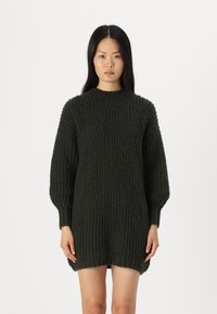 Abito maglione lavorato a maglia spessa di colore verde scuro. Presenta una texture a coste, collo alto e maniche a palloncino. Leggermente più lungo sul retro.
