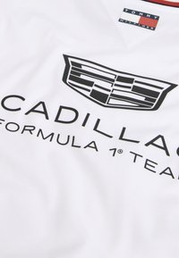 Λευκό ύφασμα με μαύρο λογότυπο Cadillac και κείμενο "Cadillac Formula 1 Team", εμφανίζοντας επίσης μικρή ετικέτα του Tommy Hilfiger στην κορυφή.