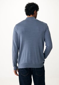 Ljusblå stickad cardigan med långa ärmar, ribbade muddar och rund halsringning, i kombination med mörka denimjeans. Slät textur.