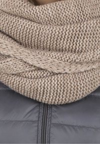 Écharpe en tricot beige clair, présentant un motif texturé et un design torsadé ; drapée autour du cou sur une veste gris foncé.