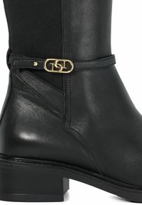 Botte en cuir noir avec une finition lisse, dotée d'un accent en métal doré et d'un panneau en tissu texturé. Design à talon carré et détails brodés.