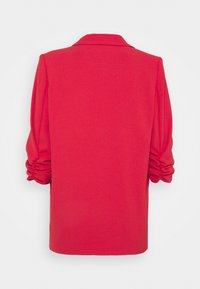 Punainen rakenteellinen bleiseri, jossa on kauluskollerot, pörröiset hihat ja kerätty yksityiskohta hihansuissa. Valmistettu pehmeästä, rakenteellisesta kankaasta.