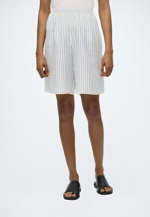 Person iført hvide shorts med tynde blå lodrette striber og sorte åbneåbne sandaletter, stående mod en hvid baggrund.