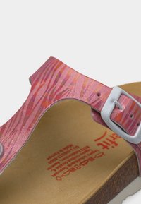 Close-up van een roze gespenbandje met patroon en een zilveren gesp, met rood gedrukt tekst op een beige voetbed en een kurken zool eronder.