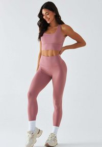 Jasnoróżowy zestaw sportowy z dopasowanym krótkim topem i legginsami z wysokim stanem wykonanymi z gładkiego materiału, zestawiony z białymi skarpetkami i kremowymi sneakersami.