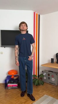 T-shirt de gola redonda azul-marinho com pequenas bordaduras florais, combinado com jeans azul de perna reta e sapatos castanhos. Design minimalista, ajuste casual.