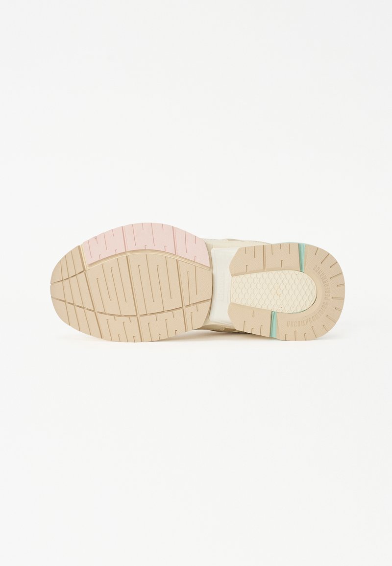 Schuh mit einer beigen Gummisohle, ausgestattet mit rosa und türkisfarbenen Akzenten, strukturierten Rillen und einem weißen rechteckigen Abschnitt an der Seite.