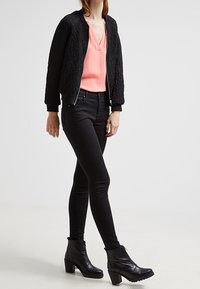 Giacca bomber nera con texture sopra una maglietta a v pesco, abbinata a jeans skinny neri e stivaletti neri con tacco grosso.