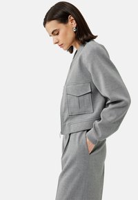 Szary bomber z zamkiem błyskawicznym, dwoma przednimi kieszeniami, ściągaczami na mankietach oraz luźnym fasonem, w zestawie z dopasowanymi szarymi spodniami.