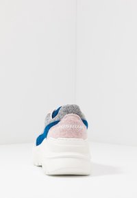 Des baskets avec une tige en feutre gris, des accents en daim bleu et un talon en feutre rose. Semelle en caoutchouc blanc avec le logo "JOSHUA" sur le talon.