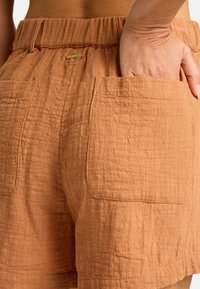 Lätta, texturerade orange shorts med elastisk midja och två stora fickor på sidorna. Guldigt logotypaccent närvarande.