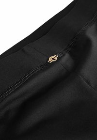 Crni materijal s glatkom teksturom, skrivenim patentnim zatvaračem i zlatnim logom uz šav. Jednostavan, elegantan dizajn.