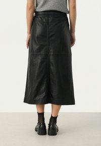 Black leather midi skirt, A-line design with visible seams, smooth texture, and a fitted waistband. Paired with black platform shoes and ankle socks.