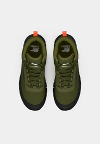 Olivengrønne sneakers med sorte såler, med en teksturert overdel, flate lisser og en oransje løftestropp på hælen for enkel påkledning.