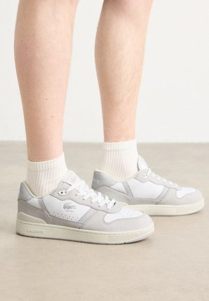 Weiße und graue Sneaker mit einem glatten Obermaterial aus Leder, perforierten Details und Gummisohle. Mit Lacoste-Logo an der Seite. Mit strukturierten Akzenten.