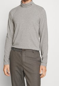 Graues langärmliges Turtleneck-Shirt aus Baumwollmischung, mit schlanker Passform und einem kleinen Logo-Detail am Hals, kombiniert mit karierten Hosen.