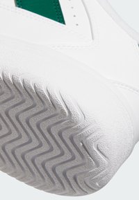 Semelle de basket blanche en caoutchouc texturé, présentant un motif en zigzag pour l'adhérence. Accent vert sur la partie supérieure près du talon.