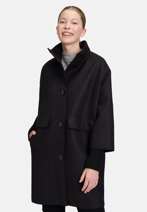 Cappotto in misto lana nero con colletto alto, grandi bottoni frontali e due tasche laterali. Presenta una silhouette rilassata e polsini a costine.