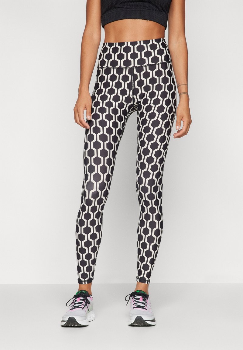 Legíny s černo-bílým vzorem mají geometrický design s hexagonálními tvary, vysoký pas a hladkou, pružnou texturu.