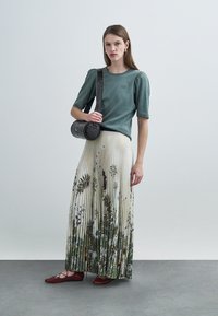 Πράσινο ριμπ κοντομάνικο τοπ, μπεζ πλισέ φλοράλ φούστα, κόκκινες μπαλαρίνες και στρογγυλή μαύρη τσάντα με λουρί. Απλή, κομψή εμφάνιση.