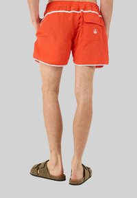 Costumi da bagno arancioni con bordi bianchi, dotati di una tasca esterna e un piccolo logo. Il tessuto è leggero e asciuga rapidamente.