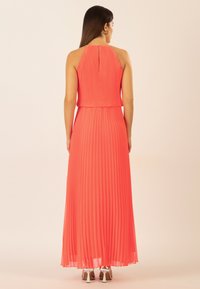 Korallfarbenes, plissiertes Maxikleid mit Trägern,details im Schlüsselbereich an der Rückseite und fließendem Stoff. Akzentuiert mit silberfarbenen High Heels.