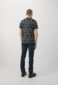 Camiseta gráfica negra con patrones de texto en blanco, de mangas cortas y ajuste relajado, combinada con jeans de color azul oscuro y calzado negro.
