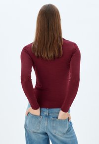 Burgundy pitkähihaisen paidan, jossa on istuva muotoilu, ribbikuvio ja pyöreä pääntie, yhdistettynä korkeavyötäröisiin sinisiin farkkuihin.