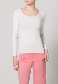 Langærmet hvid jersey top med rund halsudskæring, parret med bukser i pink med elastisk talje og en bundet bånddetalje.