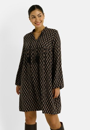 Robe noire et à motifs avec des manches longues, décolleté en V et détails à franges, offrant un corsage ajusté et une jupe évasée.