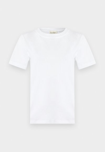 Απλό λευκό κοντομάνικο T-shirt με στρογγυλή λαιμόκοψη και μια μικρή μπεζ ετικέτα μέσα στο γιακά που γράφει "CLOSED."