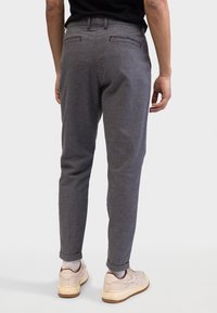 Pantalones gris espiga con un corte entallado, con cintura, dos bolsillos traseros y puños remangados, combinados con zapatillas beige.