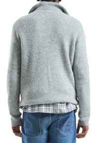 Szary prążkowany sweter z wysokim kołnierzem, strukturalnym wzorem dzianiny, długimi rękawami, noszony na koszuli w kratę, w połączeniu z niebieskimi dżinsami.