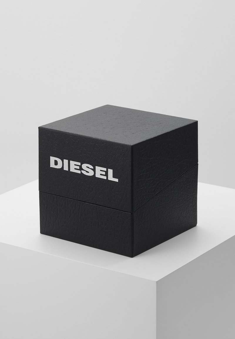 Schwarze Lederbox mit strukturiertem Finish, mit einem silbernen "DIESEL"-Logo auf der Vorderseite, quadratische Form, auf einem weißen Sockel platziert.