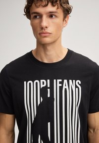 Zwarte katoenen t-shirt met een wit grafisch ontwerp met verticale lijnen en tekst, met een silhouet. Standaard ronde hals.