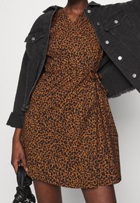 Robe à imprimé léopard marron avec une taille nouée, un col en V, des manches courtes, accompagnée d'une veste en denim noire. Texture lisse avec une coupe décontractée.