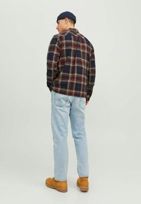 Camisa de franela en patrón de cuadros con colores azul marino, rojo y beige; de manga larga; combinada con jeans de mezclilla azul claro y botas de ante marrón.