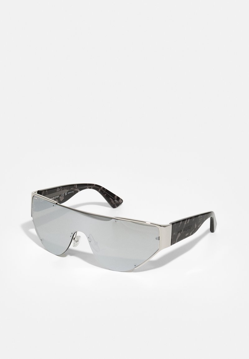 Gafas de sol con un marco de metal plateado, grandes lentes gris ahumado y patillas de plástico con un patrón de mármol negro. Presenta un diseño minimalista.
