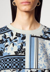 Top con motivo floreale in blu, nero e crema. Tessuto leggero, scollatura a girocollo e diverse grafiche.