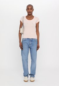 Lichtroze aansluitend T-shirt met een ronde halslijn en reliëfletters. Gepaarde met lichtblauwe rechte jeans en witte sneakers.