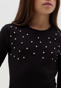Schwarzer, gerippter Pullover, der mit verstreuten silbernen Strasssteinen verziert ist, mit einem runden Ausschnitt und langen Ärmeln.