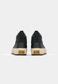 Baskets montantes noires avec un dessus texturé et une semelle de couleur crème. Présente une languette de talon avec "CONVERSE ALL STAR."
