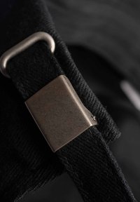 Correa negra con una superficie texturizada y un cierre metálico, con forma rectangular y un acabado plateado mate. Vista en primer plano.