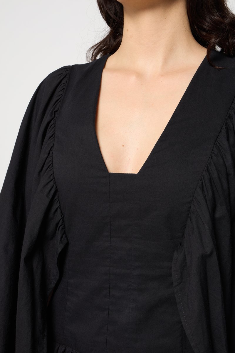 Schwarzes Kleid mit V-Ausschnitt und ausgestellt geschnittenen Ärmeln. Verfügt über einen strukturierten Stoff und Raffungselemente entlang der Schulternähte.