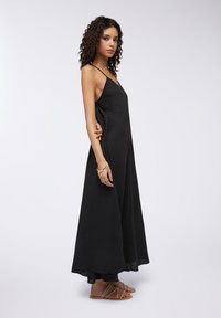 Abito lungo nero con design senza maniche, scollatura a V e silhouette fluida. Presenta un tessuto strutturato ed è abbinato a sandali con cinturino.
